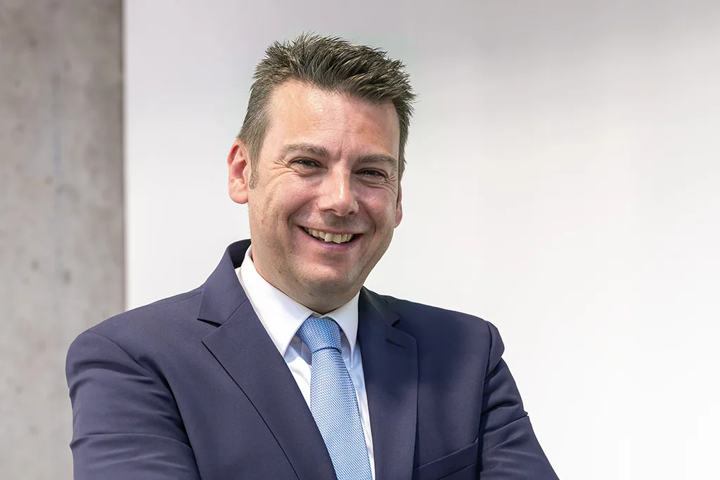 Porträtbild eines Mannes in Anzug mit hellblauer Krawatte.